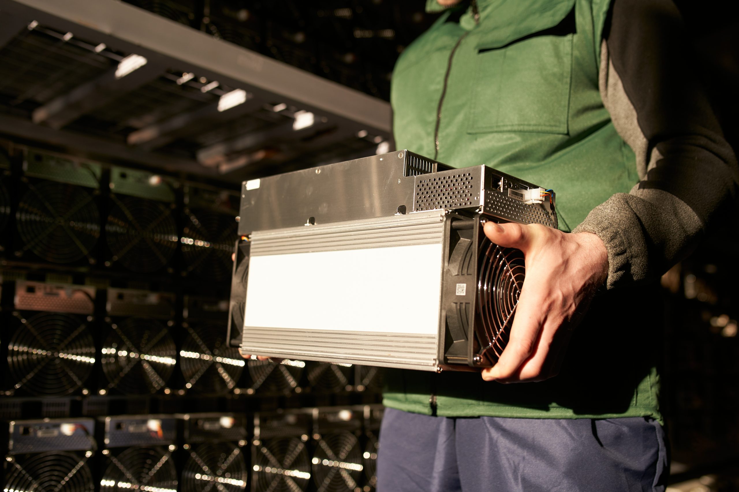 Mover holding bitcoin ASIC miner in warehouse. Worker with ASIC mining equipment on stand racks for mining cryptocurrency in steel container. Application specific integrated circuit miners storage.